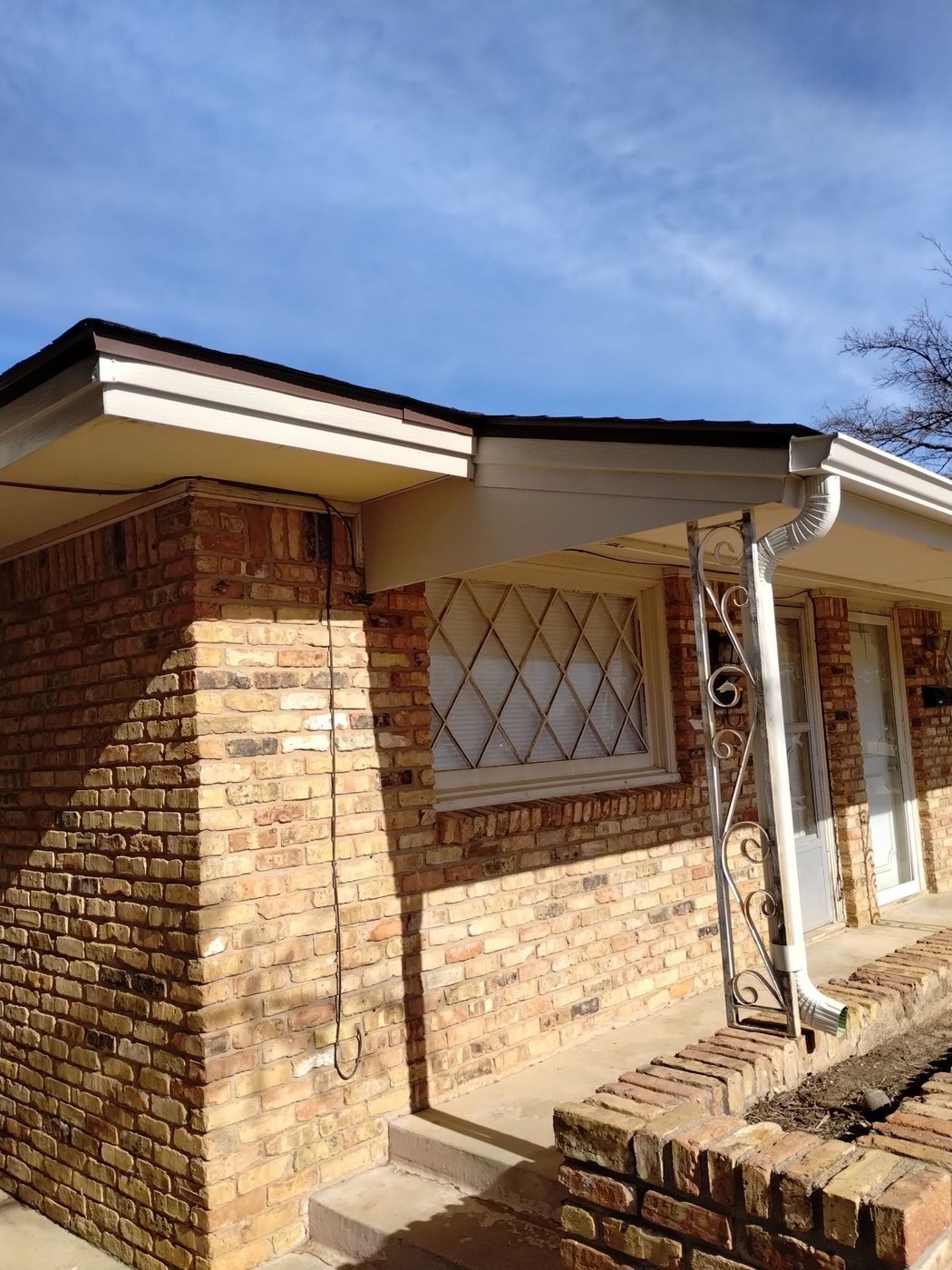 White seamless downspout with a decorative iron bracket on a Lubbock brick home