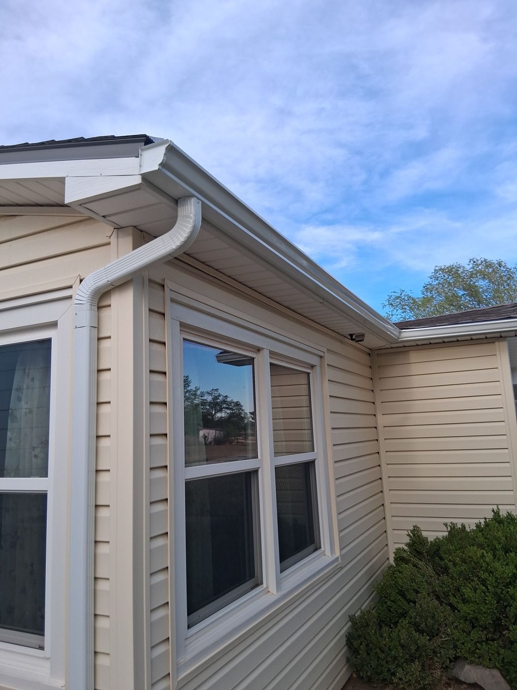A freshly installed white seamless gutter and downspout on a Lubbock home against a blue sky.